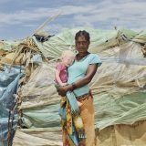Teresa, 25, and her daughter Jopondje, 2, at their shelter in Etunda Refugee Camp, Namibia. Many families weave together pieces of cardboard with small plastic bags until they form walls made up of dozens of pieces.
