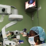 An eye surgeon has her eye operation live on a TV screen above her.